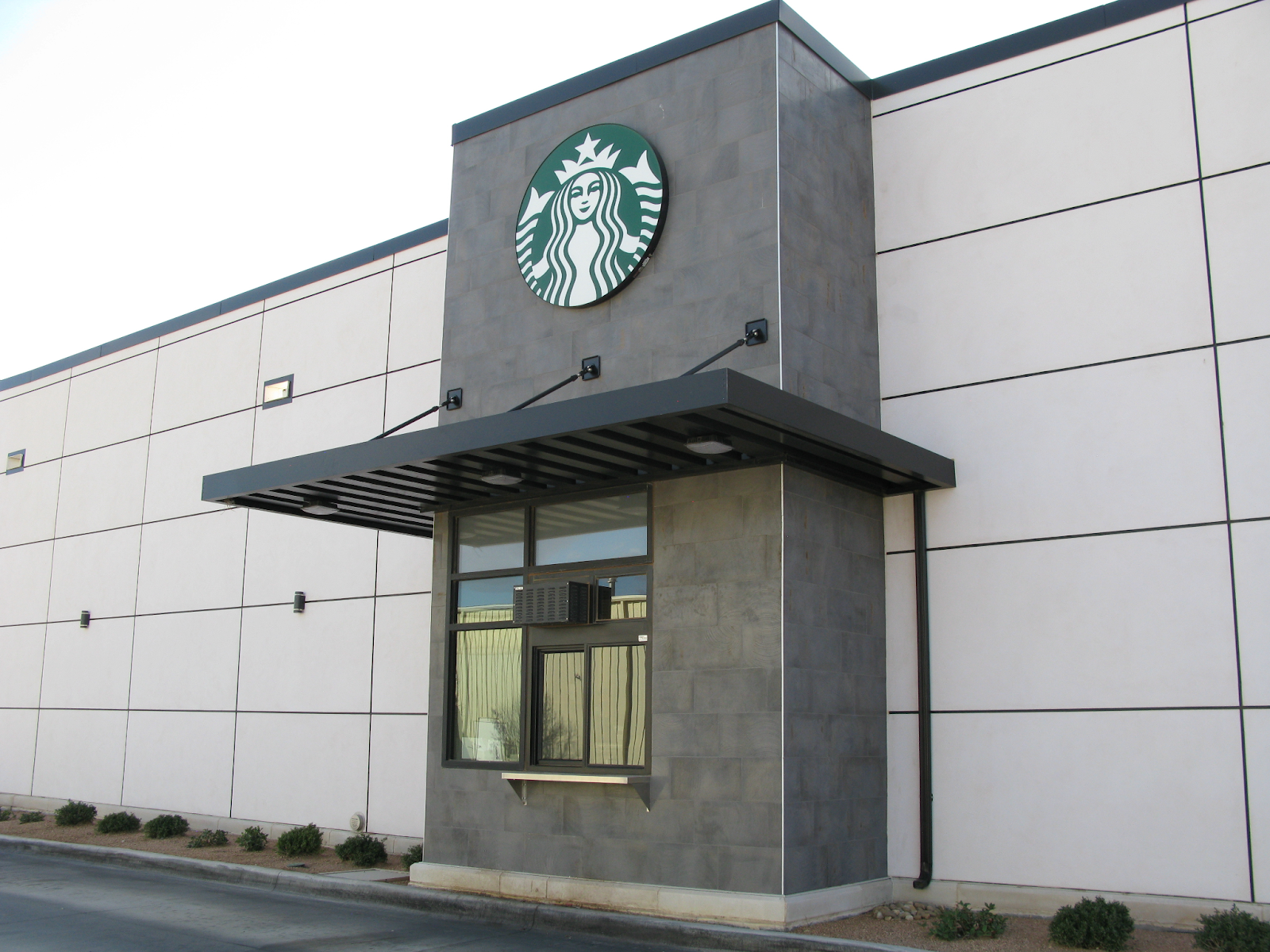 A canopy covers a drive-thru outside a Starbucks building.